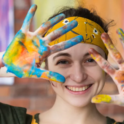 Young woman in headband showing multi-coloured painted hands to the camera